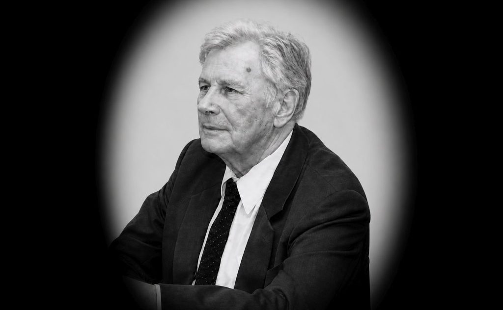 Czarno-biały portret mstarszego mężczyzny w garniturze i krawacie (owal na czarnym tle).