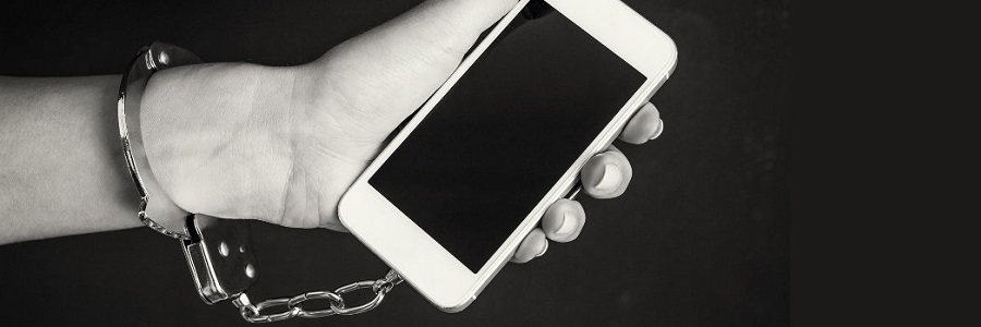 Wyciągnięta do przodu dłoń ze smartfonem, który jest przyczepiony łańcuchem do przedramienia niczym kajdanki.