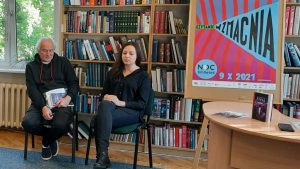 Marta Sobiecka i Tadeusz Krajewski na tle regałów z książkami. Obok plakat "Czytanie wzmacnia" z logo Noc Bibliotek i datą 9.10.2021 r. i