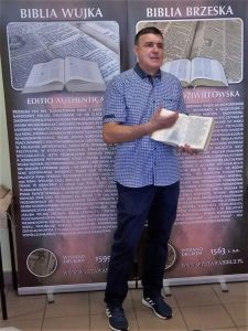 Autor wystawy na tle banerów "Biblia Wujka" i Biblia brzeska"