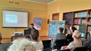 Leśnik prezentuje uczestnikom spotkania w bibliotece prezentację multimedialną na ekranie.