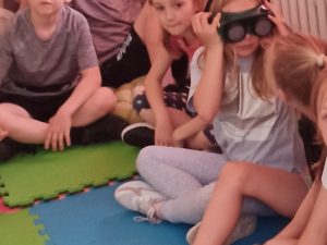Grupka dzieci siedzi na matach w czasie zajęć edukacyjnych.