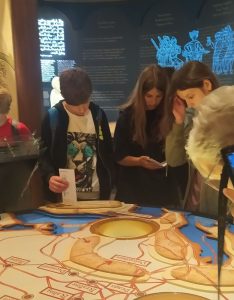 Grupka młodzieży pochyla sie nad eksponatami w muzeum historycznym.