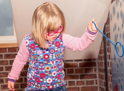 Dziewczynka z zespołem Downa w różowych okularach z zabawką w ręce.