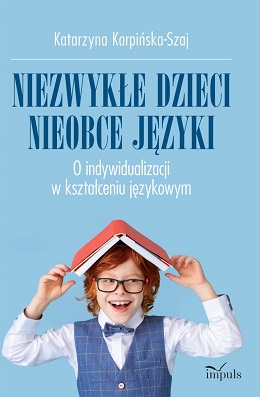 Uśmiechnięty rudy chłopiec w okularach z książką na głowie. Na okładce jeszcze nazwa autorki, tytuł i logotyp wydawnictwa.