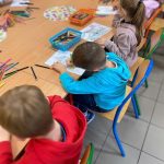 Dzieci przy stoliku kolorują obrazki.