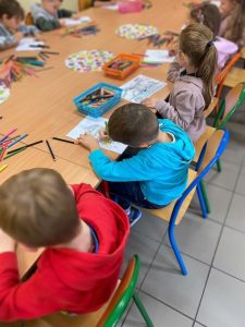 Dzieci przy stoliku kolorują obrazki.