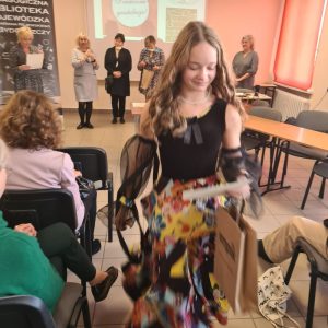 Uśmiechnięta dziewczyna wraca na swoje miejsce na sali z nagrodą.