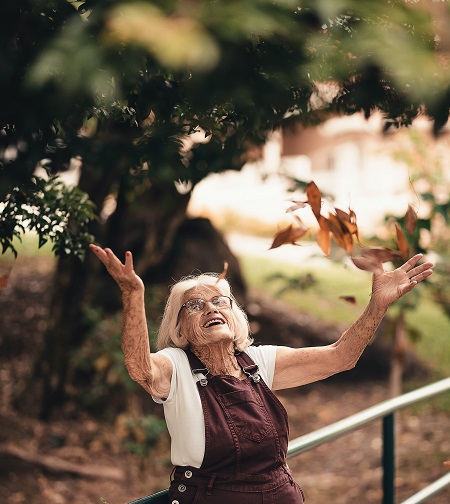Uśmiechnięta starsza kobieta rzuca liście w górę.