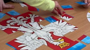Dziecięce dłonie układają puzzle z herbem narodowym.