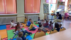 Kobieta czyta dzieciom siedzącym na kolorowych matach.