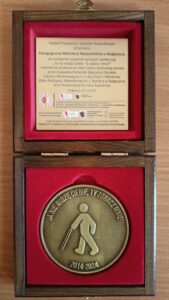 Medal w ozdobnym drewnianym opakowaniu, wyściełanym czerwonym pluszem.