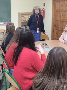 Kobieta stoi przed stolikami, przy których siedzą studentki.