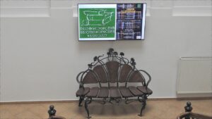 Stylowa ławka ze zdobieniami metalowymi. Nad nią ekran z logo biblioteki i programem seminarium.