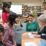 Kilka osób przy stoliku. W tle regały z książkami.