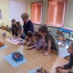 Dzieci i nauczycielka przyglądają się pracy plastycznej.