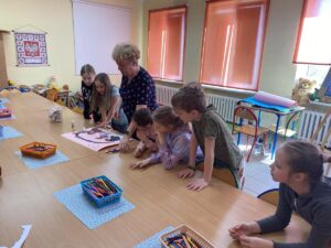 Dzieci i nauczycielka przyglądają się pracy plastycznej.