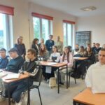 Kobieta zwrócona do sali wypełnionej młodzieżą.