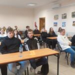 Nastolatki siedzą przy stolikach szkolnych.