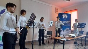 Pięcioro młodych muzyków w białych koszulach z instrumentami dętymi.