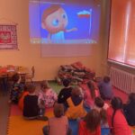 Małe dzieci siedzą na kolorowych matach i oglądają film o barwach narodowych.