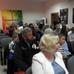 Sala z obrazami na ścianach. W środku grupa ludzi na krzesłach zwrócona w jedną stronę.