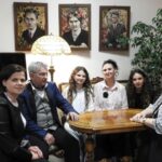 Grupa osób w scenerii w stylu secesyjnym: stara lampa, zegar obrazy, stylowe meble.