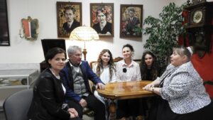 Grupa osób w scenerii w stylu secesyjnym: stara lampa, zegar obrazy, stylowe meble.