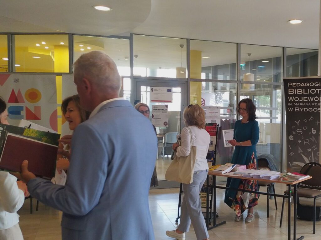 Ludzie przechodzą obok stoisk w hallu budynku.