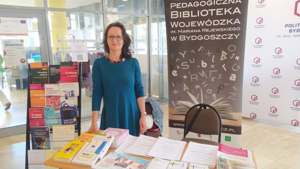 Kobieta przy stoisku z banerem Pedagogicznej Biblioteki Wojewódzkiej.