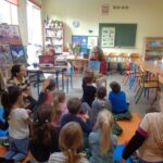 Kobieta prezentuje książkę małym dzieciom siedzącym na kolorowych matach.