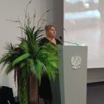 Kobieta w czarnej sukience za katedrą z orłem.