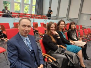 4 osoby, siedzą na krzesłach i się uśmiechają.