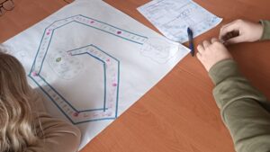Na blacie dwie kartki, jedna z wymalowaną planszą gry, druga z wypisanymi zasadami.