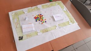 Papierowa plansza z polami gry, dwiema stertami kart z zadaniami i guzikami