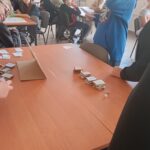 Stolik, na blacie kartonowe elementy gry, wokół młodzież.