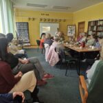 Sala pełna osób skupionych wokół stolika. Patrzą na prezentację.