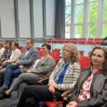 Sześć kobiet i jeden mężczyzna siedzący na krzesłach.