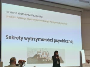 Kobieta występująca na tle slajdu z tytułem prezentacji.