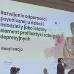 Kobieta występująca na tle slajdu z tytułem prezentacji.