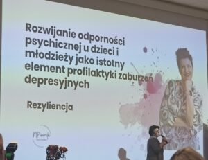 Kobieta występująca na tle slajdu z tytułem prezentacji.
