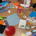 Materiały plastyczne na stoliku: kolorowe kartki, kle, tasiemki ozdobne.