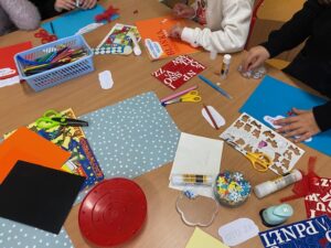 Materiały plastyczne na stoliku: kolorowe kartki, kle, tasiemki ozdobne.