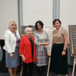 4 kobiety pozujące na tle wystawy na sztalugach.