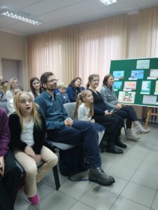 Ludzie w różnym wieku, siedzą na krzesłach w kilku rzędach.