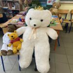 Duży biały pluszak i dwa mniejsze ustawione na krześle przy biurku.