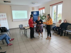 Kobieta w czerwonej marynarce, kobieta w czarnej sukience i kobieta w żółtej koszuli stoją obok siebie.