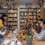 Pięć kobiet rozmawia przy stoliku na tle regałów z książkami.