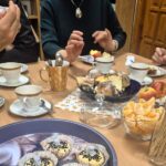 Osoby siedzące przy stoliku zastawionym ciastkami z wróżbami, owocami i napojami.