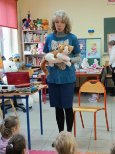 Blondwłosa kobieta stoi z maskotką kota w ręce.